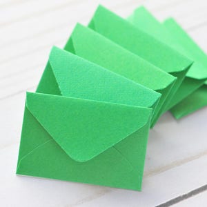 May include: A stack of bright green envelopes, folded and arranged in a fan shape on a white wooden surface.