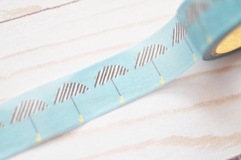 May include: A roll of blue washi tape with a repeating pattern of black and white striped umbrellas with yellow handles.