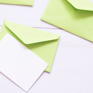 May include: A white card is placed inside a light green envelope. The envelope is folded and the flap is closed. The envelope is on a white surface.