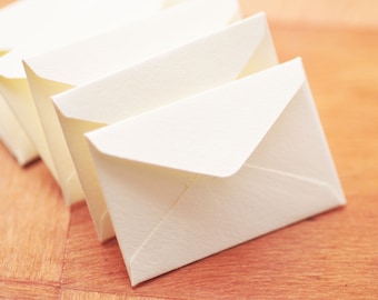 May include: A stack of white envelopes on a wooden surface. The envelopes are folded and ready to be used for sending letters or cards.