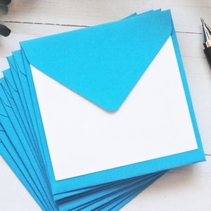 May include: A stack of light blue envelopes with white interiors. The envelopes are folded in half and have a flap on the top. The envelopes are arranged in a fan shape.