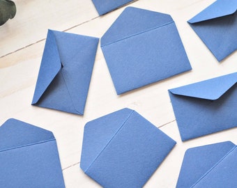 May include: A collection of eight blue envelopes of various sizes, arranged on a white wooden surface.