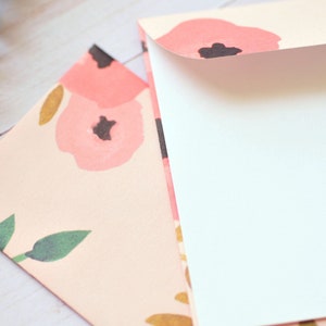 May include: Two envelopes, one with a floral pattern and the other with a white interior. The floral envelope has a pink background with pink and gold flowers and green leaves.
