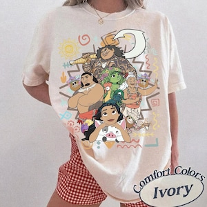 May include: An ivory short-sleeve t-shirt featuring a colorful graphic print of various animated characters, including a large figure holding a hook, a small pig, and other figures. The design includes geometric shapes and symbols in yellow, orange, and blue.