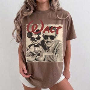 May include: Brown t-shirt featuring a vintage graphic of Walt Disney and Mickey Mouse wearing sunglasses. The word "Walt" is in red script above the image. The shirt has a classic, relaxed fit.