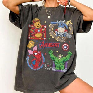 Puede incluir: Camiseta gris oscuro con personajes de dibujos animados que mezclan superh&eacute;roes de los Vengadores. Winnie the Pooh como Iron Man, Eeyore como Thor, Piglet como Spider-Man y un personaje verde parecido a Hulk. La palabra "Avengers" est&aacute; impresa en azul.