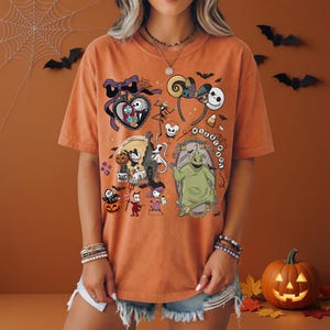 May include: An orange short-sleeve t-shirt featuring a graphic print of characters from The Nightmare Before Christmas, including Jack Skellington, Sally, Oogie Boogie, and Zero, along with various Halloween-themed icons and the text Nightmare.