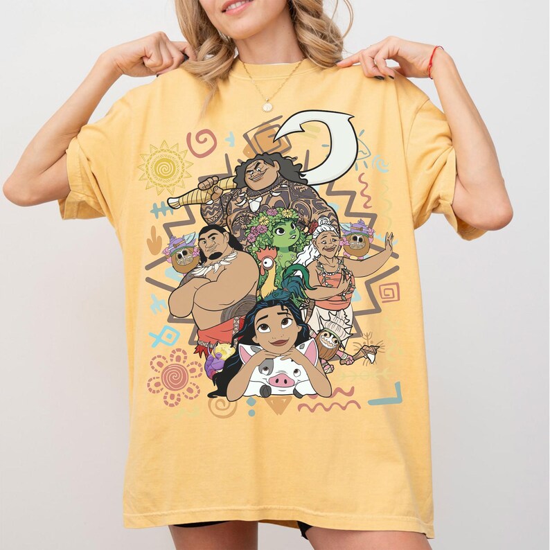 May include: A yellow short-sleeve t-shirt featuring a large graphic print of characters from the movie Moana, including Moana, Maui, Pua, Heihei, and Gramma Tala, surrounded by various colorful tribal-inspired symbols and patterns.