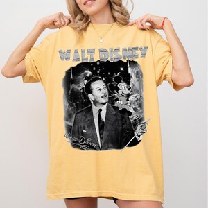 Peut inclure: T-shirt jaune moutarde avec un graphisme en noir et blanc de Walt Disney et Mickey Mouse. Le texte "WALT DISNEY" est en haut dans une police textur&eacute;e, avec la signature de Walt Disney en dessous. Le t-shirt est de style d&eacute;contract&eacute;.