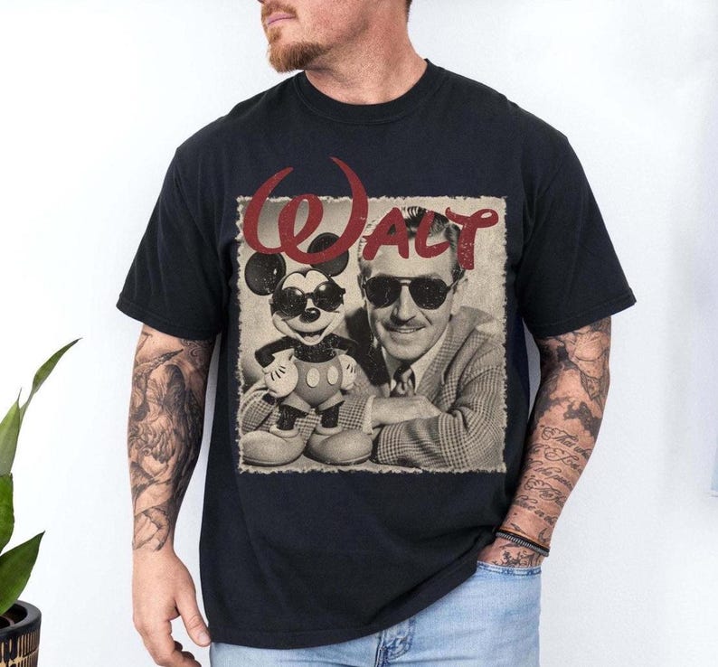 May include: Black t-shirt featuring a sepia-toned image of Walt Disney and Mickey Mouse wearing sunglasses. The word "WALT" is printed in red above the image. The shirt is a classic crew neck style.