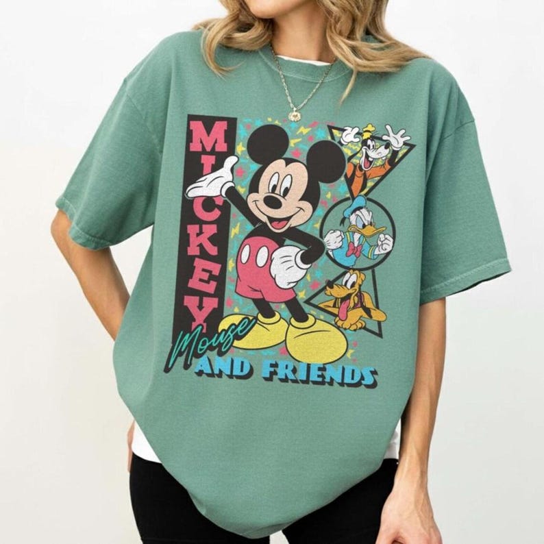 May include: A green t-shirt featuring Mickey Mouse and friends. The graphic includes Mickey Mouse in a red and white outfit, with Donald Duck, Goofy, and Pluto. The text "Mickey Mouse and Friends" is also displayed.