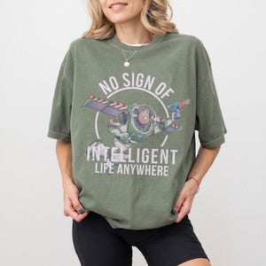 Pu&ograve; includere: T-shirt verde oliva con grafica di Buzz Lightyear in volo e la scritta bianca &laquo;NO SIGN OF INTELLIGENT LIFE ANYWHERE&raquo;. La maglietta ha maniche corte e una vestibilit&agrave; ampia, adatta per l'uso quotidiano.