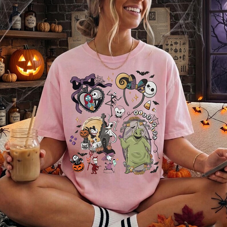 May include: A light pink t-shirt featuring a graphic print of characters from The Nightmare Before Christmas, including Jack Skellington, Sally, and Oogie Boogie, surrounded by various Halloween-themed icons like bats, pumpkins, and spiderwebs.