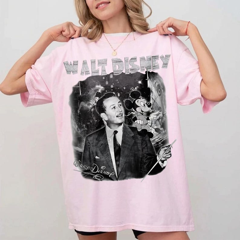 Peut inclure: T-shirt rose clair avec un imprim&eacute; noir et blanc de Walt Disney et Mickey Mouse. Le texte "WALT DISNEY" est imprim&eacute; en haut en argent&eacute;. Le t-shirt a des manches courtes et une coupe ample.