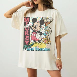 May include: Cream-colored oversized t-shirt featuring a graphic of Mickey Mouse and friends. The design includes Mickey Mouse, Goofy, Donald Duck, and Pluto. The text "Mickey Mouse and Friends" is also printed on the shirt.