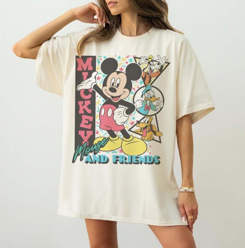 May include: Cream-colored oversized t-shirt featuring a graphic of Mickey Mouse and friends. The design includes Mickey Mouse, Goofy, Donald Duck, and Pluto. The text "Mickey Mouse and Friends" is also printed on the shirt.