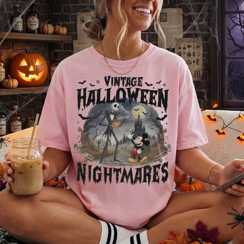 K&ouml;nnte beinhalten: Ein hellrosa T-Shirt mit einem Grafikdruck und dem Text VINTAGE HALLOWEEN NIGHTMARES. Die Illustration zeigt eine skelettartige Figur und eine Zeichentrickmaus auf einem Pfad vor einer dunklen Burg unter einem Vollmond mit Flederm&auml;usen.