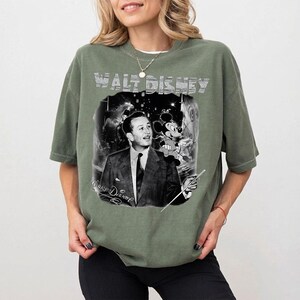 Peut inclure: T-shirt vert olive avec un imprim&eacute; noir et blanc de Walt Disney et Mickey Mouse. Le texte "WALT DISNEY" est imprim&eacute; en haut. Le t-shirt a des manches courtes et une coupe d&eacute;contract&eacute;e, id&eacute;al pour un usage quotidien.