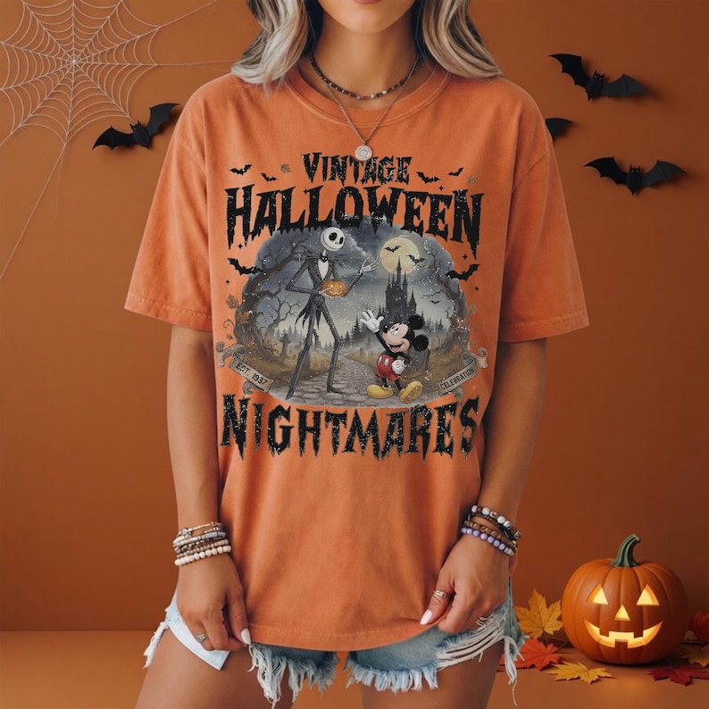 K&ouml;nnte beinhalten: Ein orangefarbenes Kurzarm-T-Shirt mit einem Grafikdruck und dem Text VINTAGE HALLOWEEN NIGHTMARES. Das Design zeigt Jack Skellington und Mickey Mouse in einer gruseligen Landschaft mit Schloss, Flederm&auml;usen und dem Text EST. 1937 CELEBRATION.