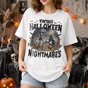 K&ouml;nnte beinhalten: Ein wei&szlig;es Kurzarm-T-Shirt mit einem Grafikdruck und dem Text VINTAGE HALLOWEEN NIGHTMARES. Das Design zeigt Jack Skellington und Mickey Mouse in einer dunklen, gruseligen Landschaft mit einem Schloss, Flederm&auml;usen und einem Vollmond.