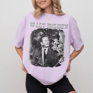 Peut inclure: T-shirt lilas avec un graphisme noir et blanc de Walt Disney et Mickey Mouse. Le texte "WALT DISNEY" est imprim&eacute; en haut, avec "Walt Disney" en script en dessous. Le t-shirt a des manches courtes.