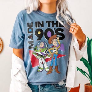May include: Blue t-shirt with the text "MADE IN THE 90'S" and cartoon images of Buzz Lightyear and Woody. The shirt has a vintage, faded look.