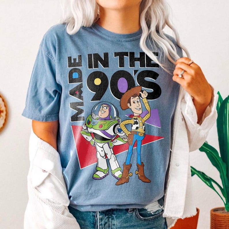May include: Blue t-shirt with the text "MADE IN THE 90'S" and cartoon images of Buzz Lightyear and Woody. The shirt has a vintage, faded look.