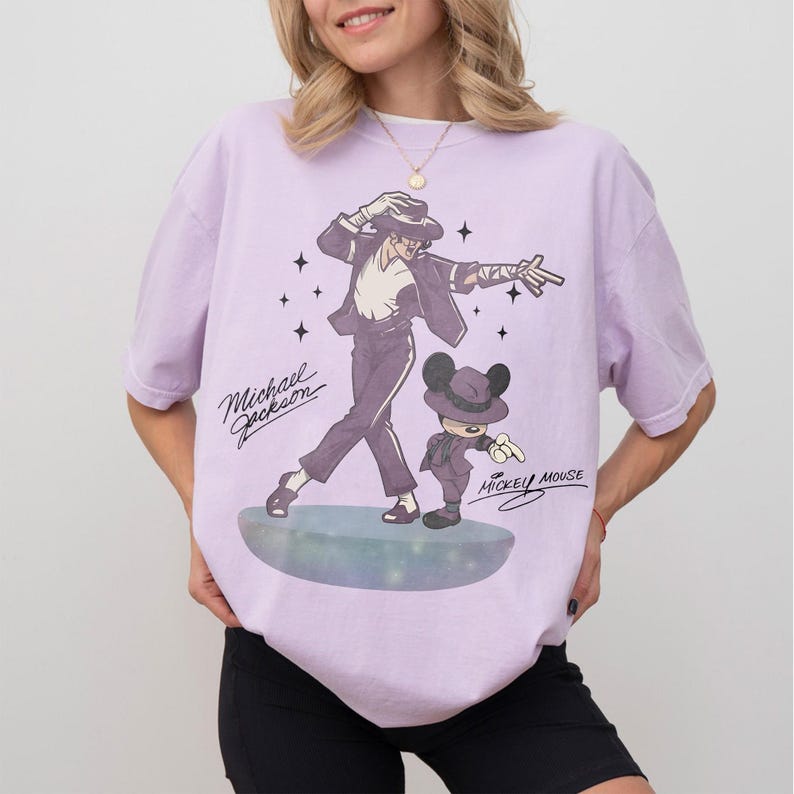 May include: Lilac-colored t-shirt featuring a graphic of Michael Jackson and Mickey Mouse in matching outfits. The design includes the text "Michael Jackson" and "Mickey Mouse" in a vintage style. The shirt is a relaxed fit.