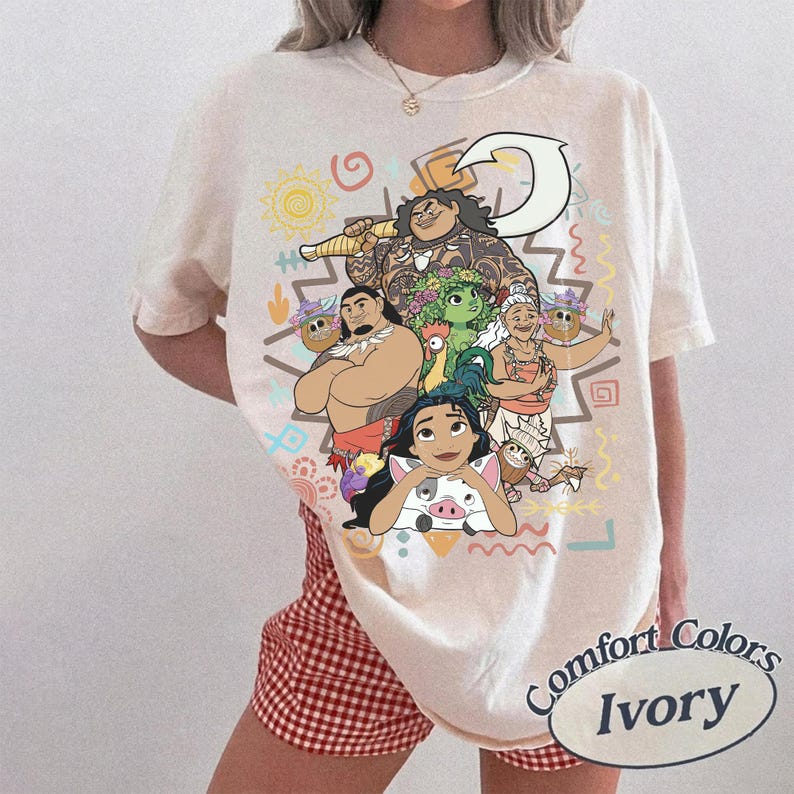 May include: An ivory short-sleeve t-shirt featuring a colorful graphic print of various animated characters, including a large figure holding a hook, a small pig, and other figures. The design includes geometric shapes and symbols in yellow, orange, and blue.