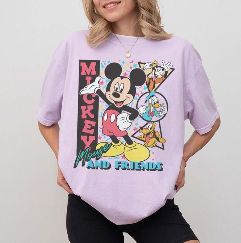 May include: A light purple t-shirt featuring Mickey Mouse and friends. The graphic includes Mickey Mouse, Donald Duck, Goofy, and Pluto. The text "Mickey Mouse and Friends" is displayed in a colorful font.