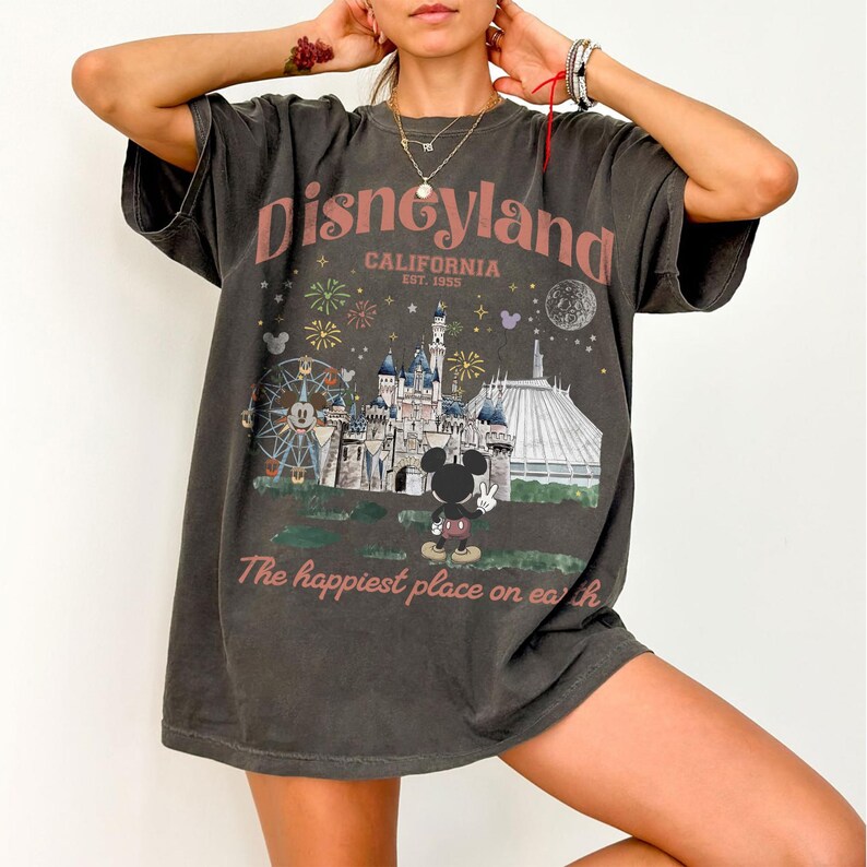 Puede incluir: Camiseta gris oscuro con un gr&aacute;fico de Disneyland. El gr&aacute;fico presenta el logotipo de Disneyland, un castillo, fuegos artificiales, Mickey Mouse y el texto "The happiest place on earth."