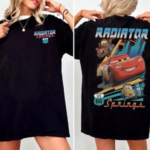May include: A black t-shirt featuring a small Radiator Springs logo on the front chest. The back displays a large graphic of Lightning McQueen, Mater, and other characters from the movie Cars, with the text Radiator Springs and US 66.