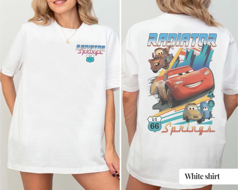 May include: A white t-shirt featuring a small Radiator Springs US 66 logo on the front chest. The back displays a large graphic of Lightning McQueen, Mater, and other characters with the text Radiator Springs and a US 66 road sign emblem.