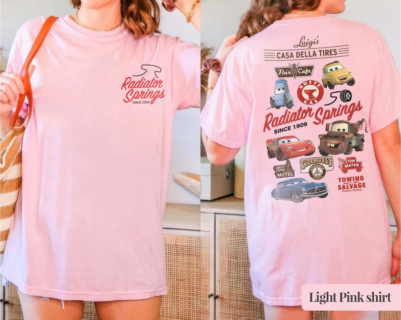 May include: A light pink t-shirt featuring a small Radiator Springs logo on the front. The back displays a large graphic with various cartoon car characters, the text Luigi's Casa Della Tires, Radiator Springs Since 1909, and Tow Mater.