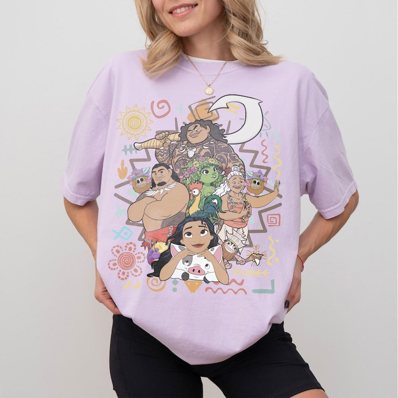 May include: A light purple short-sleeve t-shirt featuring a colorful graphic print of various animated characters, including a large figure holding a hook, a pig, a chicken, and several other figures, surrounded by small decorative shapes and symbols.