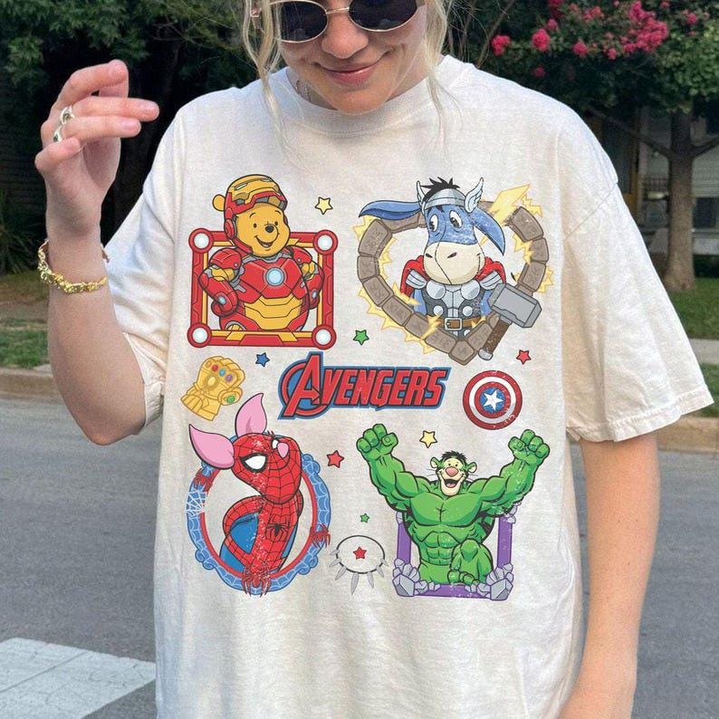 Puede incluir: Camiseta color crema con mashups de dibujos animados de personajes de los Vengadores. Se muestran Iron Man Winnie the Pooh, Thor Donkey, Spider-Pig y Hulk. La palabra "Avengers" est&aacute; impresa en rojo en la camiseta.
