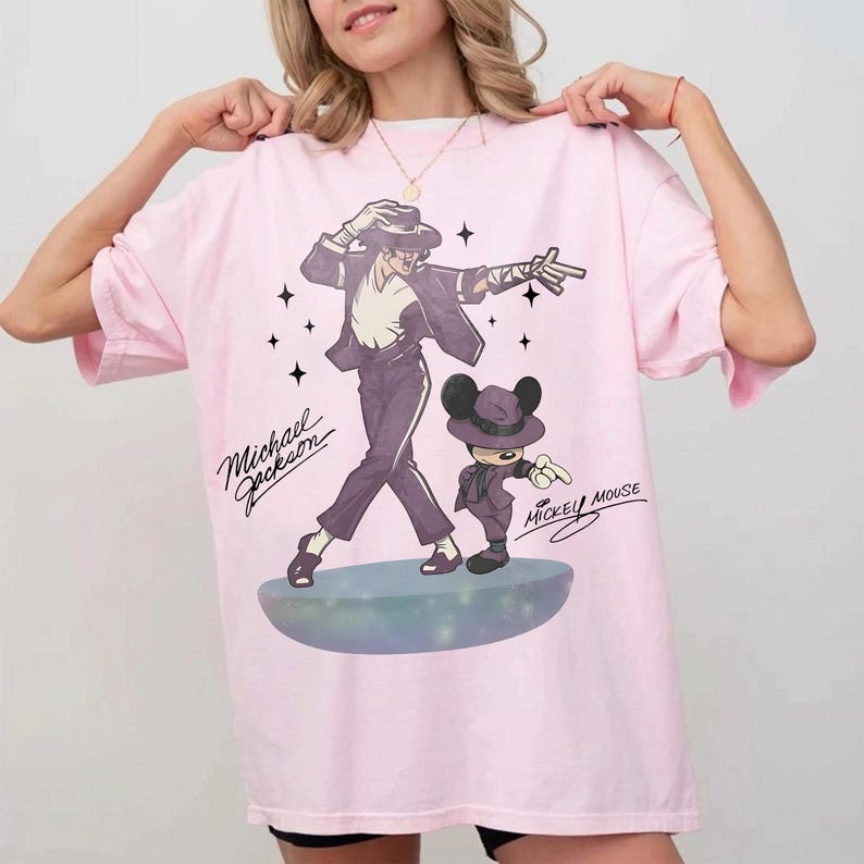 May include: Light pink t-shirt featuring a graphic of Michael Jackson and Mickey Mouse in matching outfits. The design includes the text "Michael Jackson" and "Mickey Mouse" in a script font, with star accents.