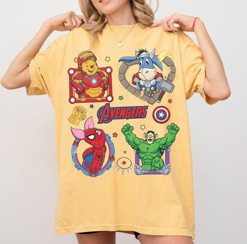Puede incluir: Camiseta amarilla con mashups de dibujos animados de personajes de los Vengadores. La camiseta incluye im&aacute;genes de Winnie the Pooh como Iron Man, un burro como Thor, Piglet como Spider-Man y Hulk. La palabra "Avengers" est&aacute; impresa en la parte delantera.