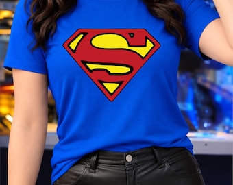 May include: A bright blue short-sleeved t-shirt featuring the iconic Superman logo on the chest. The graphic is a diamond-shaped emblem with a bold red background and a yellow S-shaped symbol outlined in red, centred on the front of the shirt.