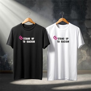 May include: Two t-shirts, one black and one white, each with the text "STAND UP TO RACISM" in white and a pink graphic. The shirts are displayed on wooden hangers.