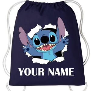 Peut inclure: Sac à cordon de serrage bleu marine avec un personnage de dessin animé. Le personnage bleu, avec de grands yeux et un large sourire, semble sortir d'un effet de papier déchiré blanc. Le texte "YOUR NAME" est imprimé en blanc.