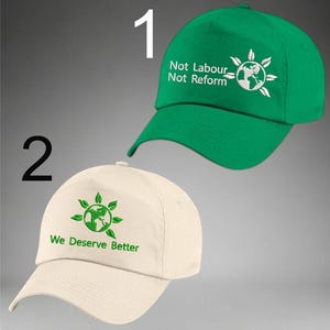 May include: Two baseball caps. One is green with the text "Not Labour Not Reform" and a globe design. The other is off-white with the text "We Deserve Better" and a globe design. Both caps have a curved peak.