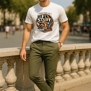 Può includere: T-shirt bianco con la scritta "That's What I Do, I Fix Stuff and I Know Things" in un design circolare con strumenti. La persona indossa pantaloni verde oliva e scarpe da ginnastica bianche. Lo sfondo è una scena sfocata all'aperto.