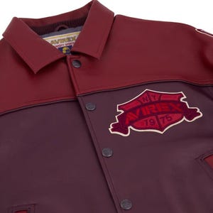 Pode incluir: Casaco de couro bord&ocirc; e marrom com fecho de bot&otilde;es e gola. O casaco apresenta um patch com o texto "AVIREX VARSITY SPORTS NY 1975".