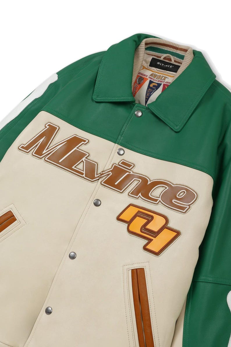 May include: A green and cream-colored varsity jacket with the word "Mlvince" in brown lettering. The jacket has a green collar and trim, with a cream-colored body and brown accents. The number "27" is displayed in orange.