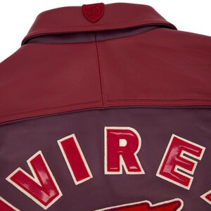 Pode incluir: Close-up de uma jaqueta de couro bord&ocirc; com gola e ombreiras em vermelho escuro contrastante. A jaqueta apresenta a palavra "VIRE" em letras grandes, vermelhas e contornadas nas costas. Um pequeno emblema &eacute; costurado na gola.