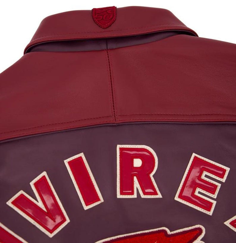 Pode incluir: Close-up de uma jaqueta de couro bord&ocirc; com gola e ombreiras em vermelho escuro contrastante. A jaqueta apresenta a palavra "VIRE" em letras grandes, vermelhas e contornadas nas costas. Um pequeno emblema &eacute; costurado na gola.