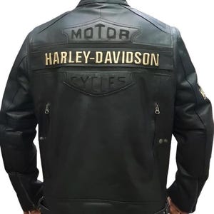 Könnte beinhalten: Schwarze Motorradjacke aus Leder mit dem Harley-Davidson-Logo auf dem Rücken. Die Jacke trägt die Worte "MOTOR HARLEY-DAVIDSON CYCLES" in Gold. Die Jacke hat Reißverschlüsse an den Ärmeln und Taschen.