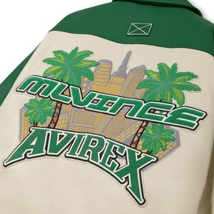 May include: Cream-colored jacket with a green collar and back panel. The back features a patch with the text "MLVINEE AVIREX" in green, along with a cityscape and palm trees.