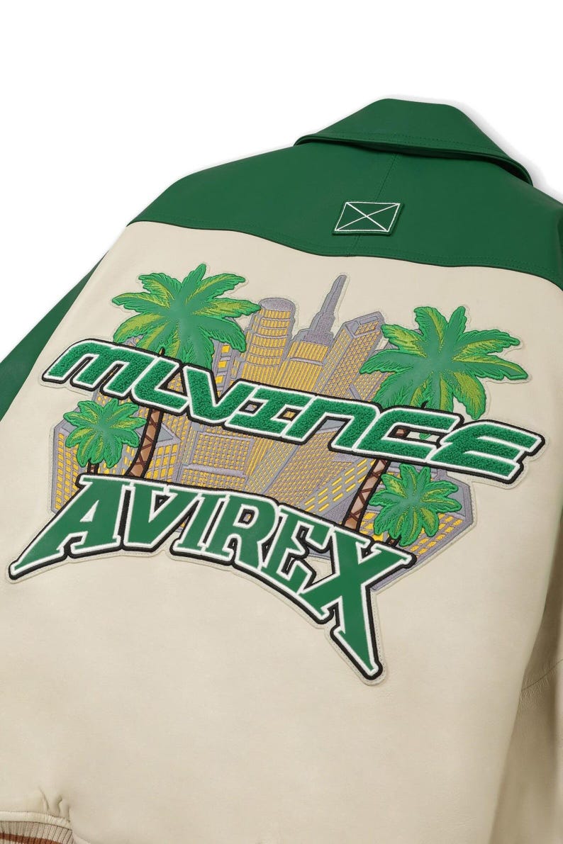 May include: Cream-colored jacket with a green collar and back panel. The back features a patch with the text "MLVINEE AVIREX" in green, along with a cityscape and palm trees.